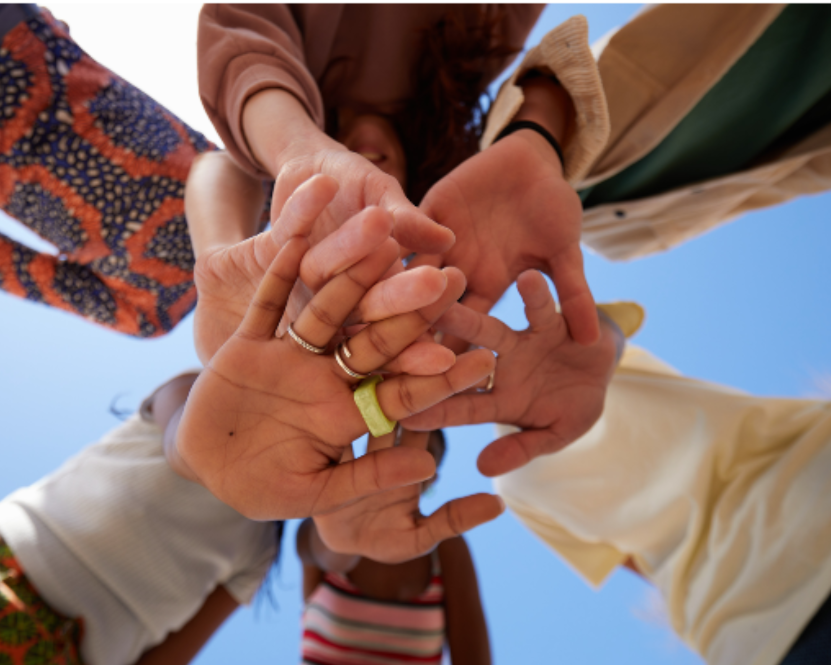 Multiple hands stacked together against a blue sky