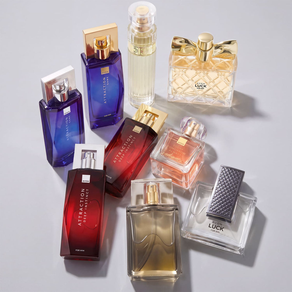 A collection of Avon perfume bottles  arranged on a light gray surface. The collection includes various colored fragrances in shades of blue, red, gold, and clear glass.
