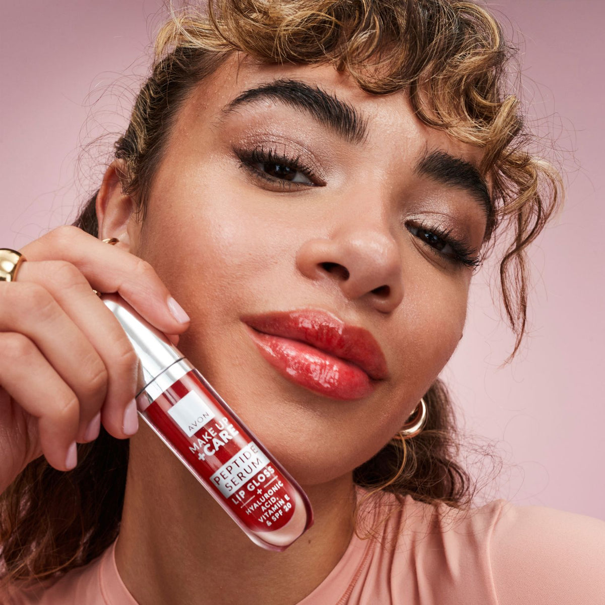 Woman holding a red lip gloss with a pink background